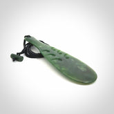 This is a sleek and slender hand carved New Zealand Jade mere pendant. The stone is a very dark green with mottled pale inclusions. The cord is black and adjustable. The pendant has a light polish and just glows. Hand carved by Kerry Thompson. One only pendant.